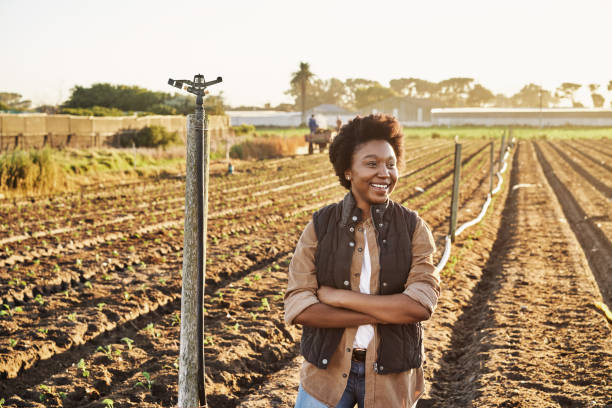 Portrait of young beautiful woman standing outdoor in field at big tractor and smiling to camera. Nice pretty female agriculture worker outdoor. Agricultural concept. a young Nigerian woman feels happy working on farm